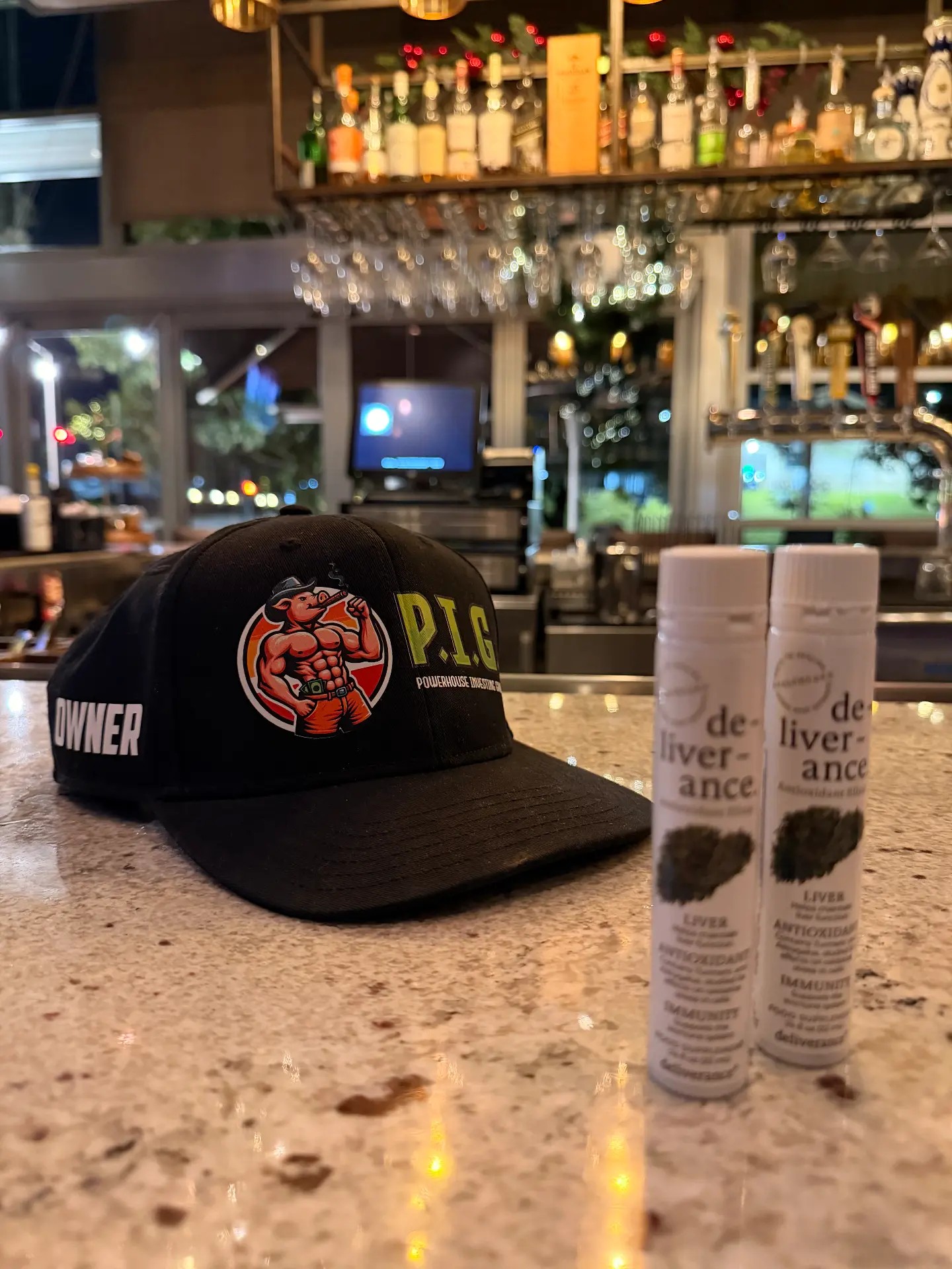 P.I.G. owner hat with De-Liver-Ance elixirs on a bar top